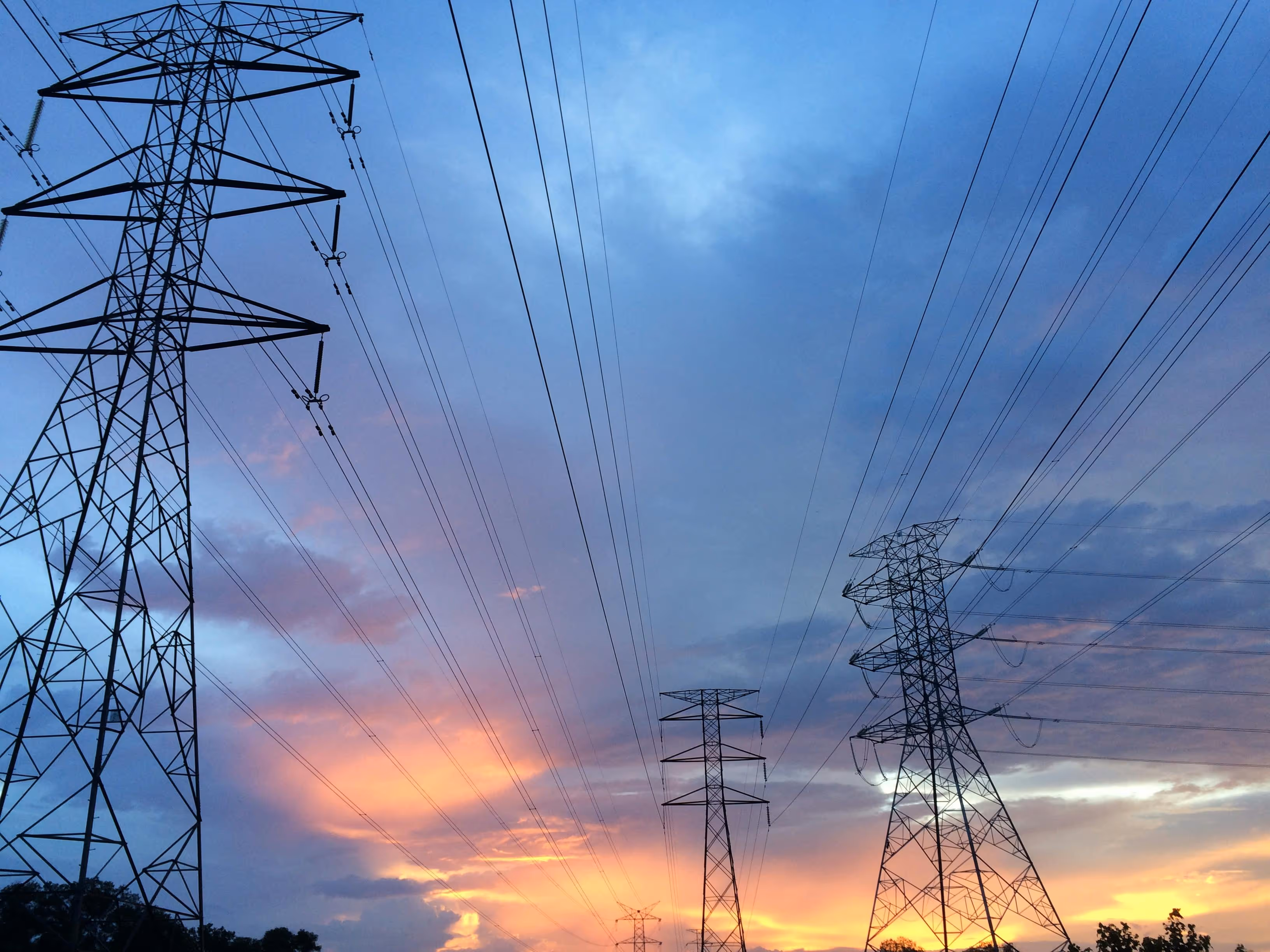Several electricity transmission towers with power lines stretching against a colorful sunset sky.