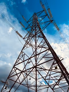 Low-angle view of a tall metal electricity transmission tower against a blue sky with scattered clouds.